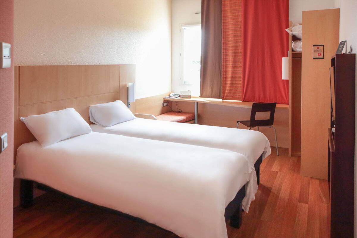 Ein Hotelzimmer mit zwei Betten, einem Schreibtisch, einem Stuhl und einem Kleiderschrank.