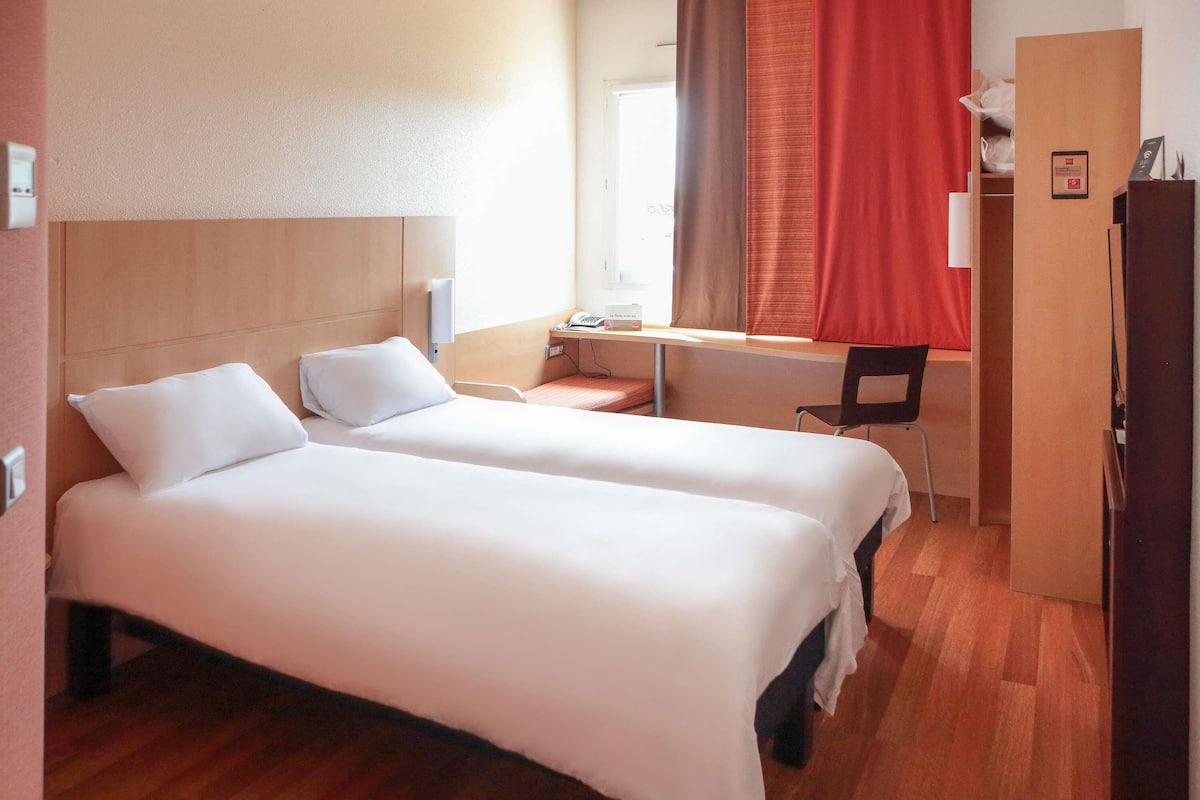 A hotel room with two beds, a desk, a chair, and a wardrobe.