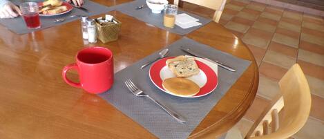 A wooden dining table with a red plate, a red mug, and a bowl of cereal.