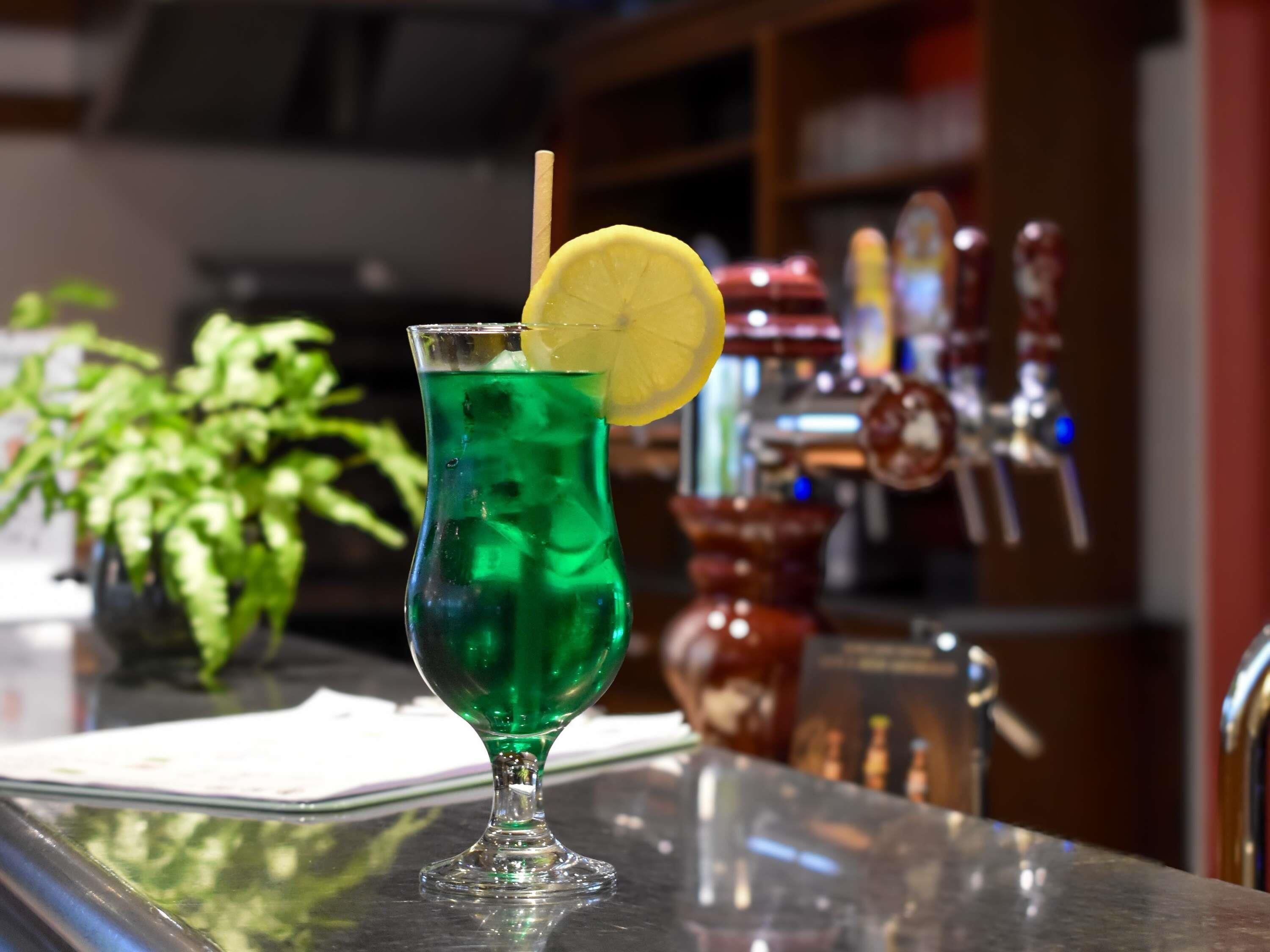 A green cocktail with a lemon slice garnish on a bar counter.