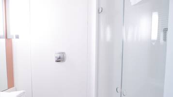 Un baño moderno con cabina de ducha de vidrio, inodoro blanco y suelo de madera.