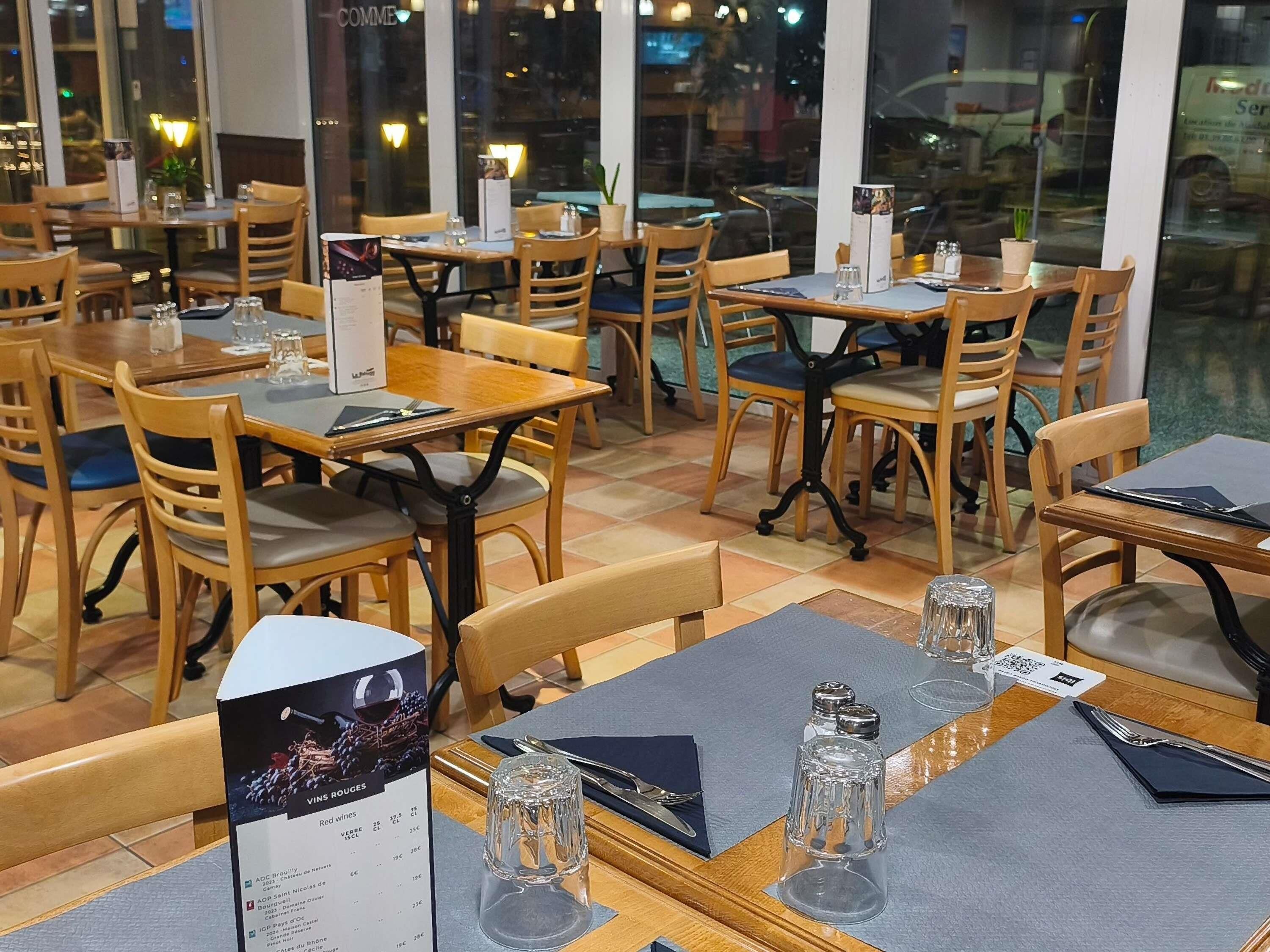 A restaurant interior with wooden tables and chairs, menus, and salt and pepper shakers on the tables.