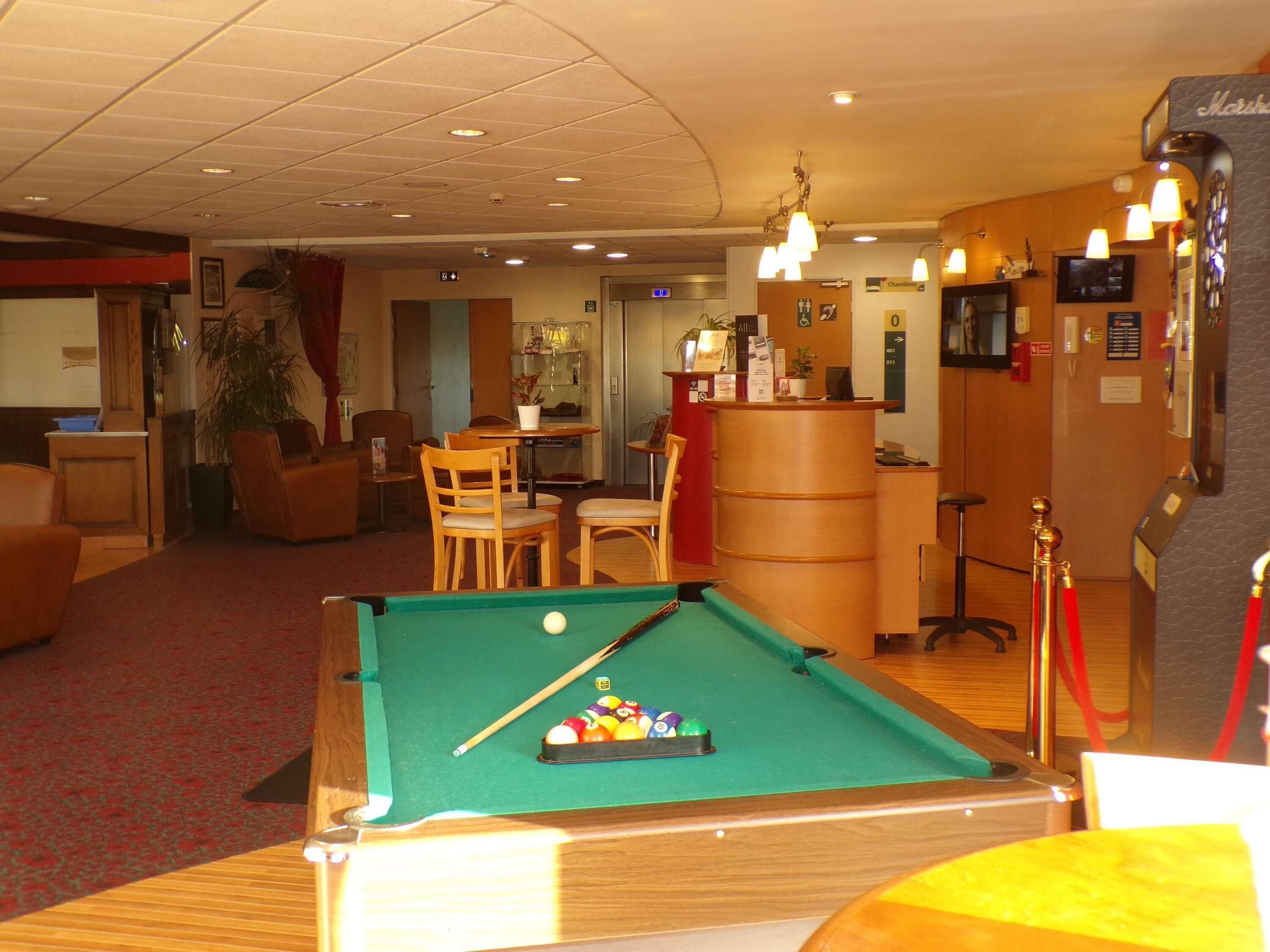 Une table de billard avec des billes, un comptoir d’accueil, un coin repas avec des chaises et une table, et un bar équipé d’un téléviseur.