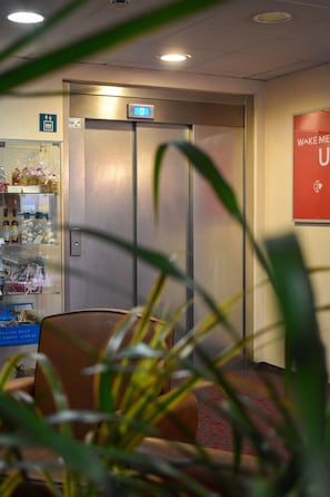 Welcome to the hotel lobby, featuring a central elevator, vending machine, and comfortable seating area.