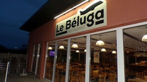 El exterior del restaurante Le Béluga con un letrero sobre la entrada, grandes ventanales de vidrio y mesas al aire libre visibles en el interior.