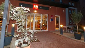 Entrada de un hotel con un letrero rojo, puertas de vidrio y plantas en macetas.