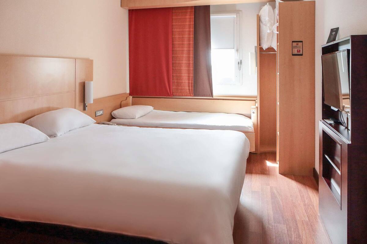 Ein Hotelzimmer mit zwei Betten, einem Fernseher, einem Kleiderschrank und einem Fenster mit Vorhängen.