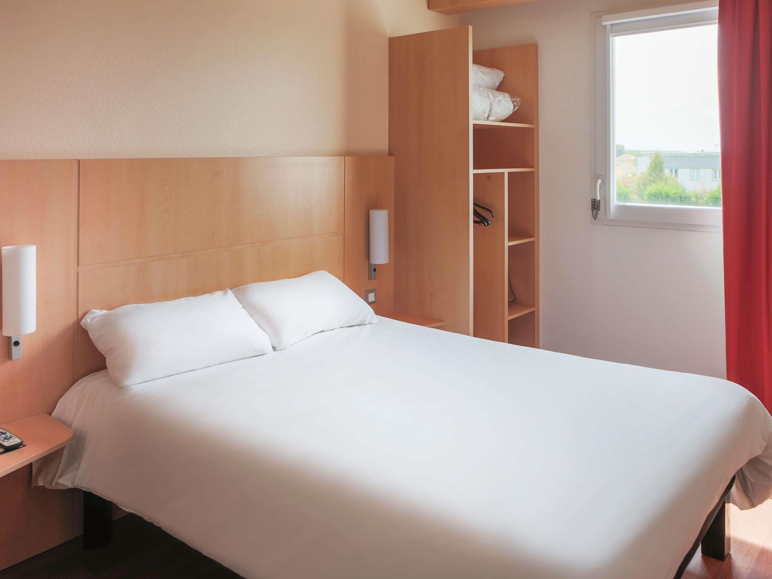 A hotel room with a bed, a nightstand, a wardrobe, and a window with curtains.