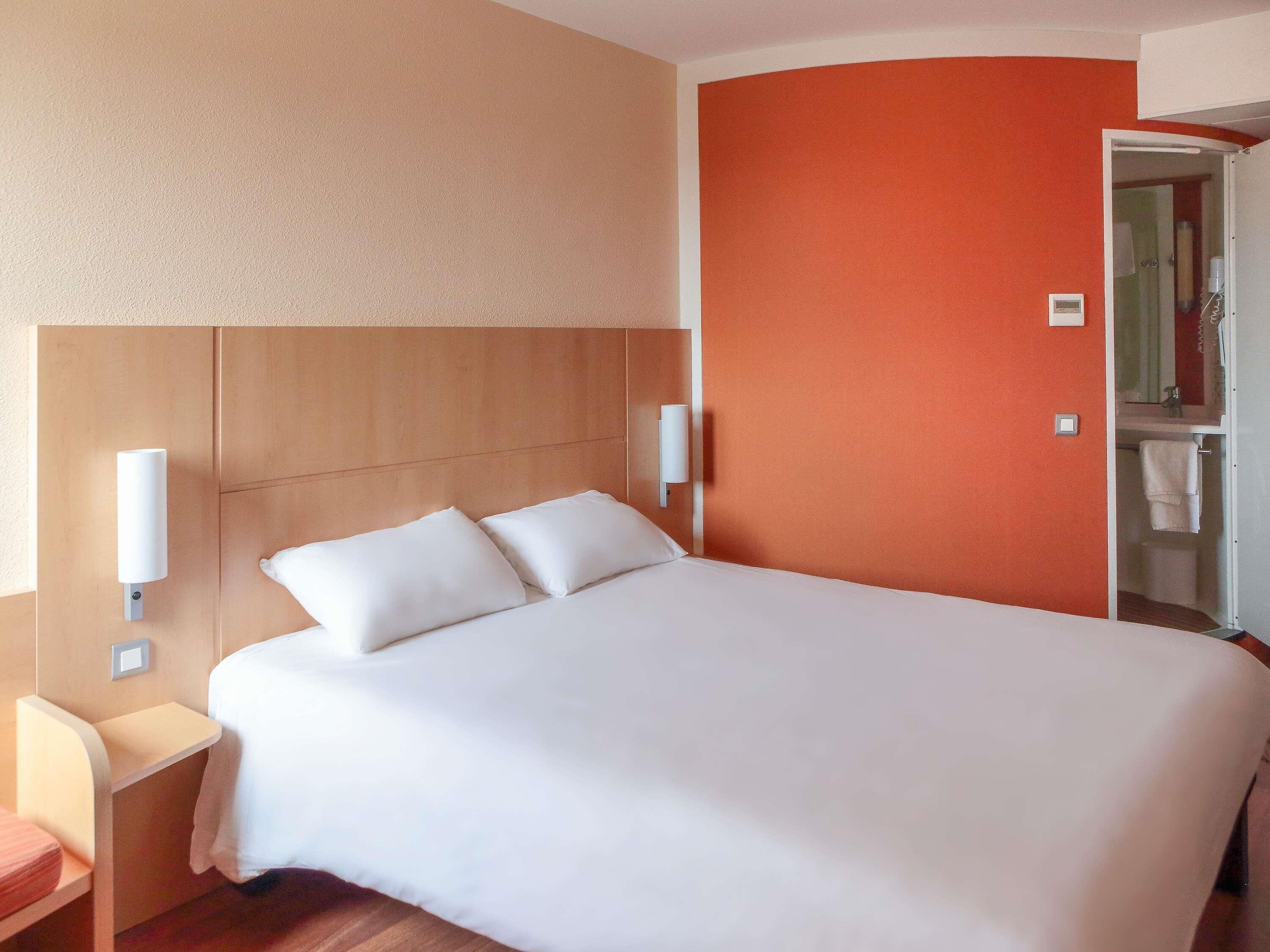 Una habitación de hotel con cama, mesitas de noche y un baño visible a través de una puerta abierta.