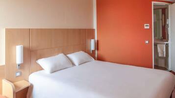 Una habitación de hotel con cama, mesitas de noche y un baño visible a través de una puerta abierta.