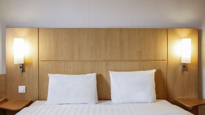 Habitación de hotel con cabecera de madera, dos almohadas blancas y lámparas de noche.