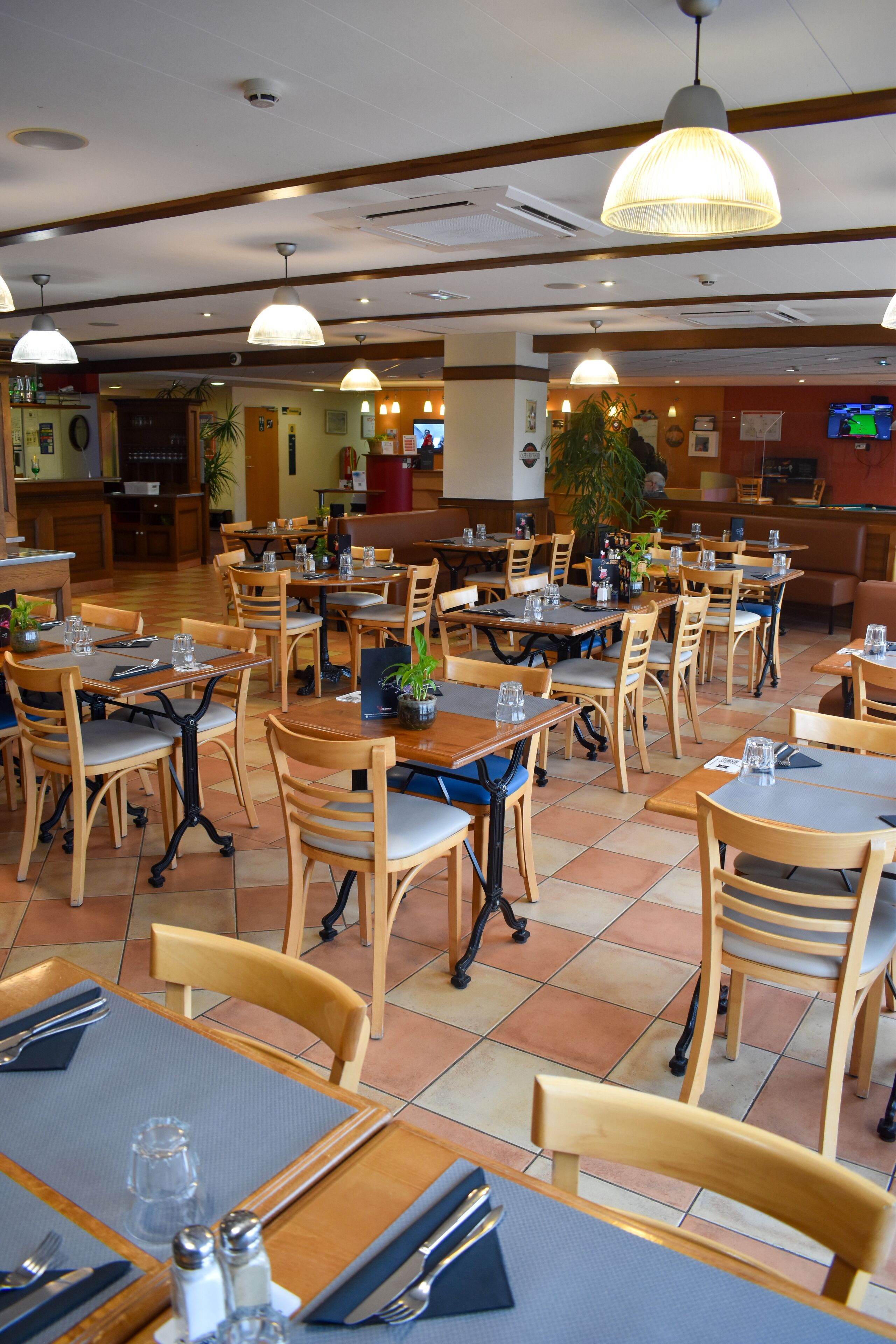 Un restaurante con mesas y sillas de madera, una zona de bar y una pantalla de televisión.