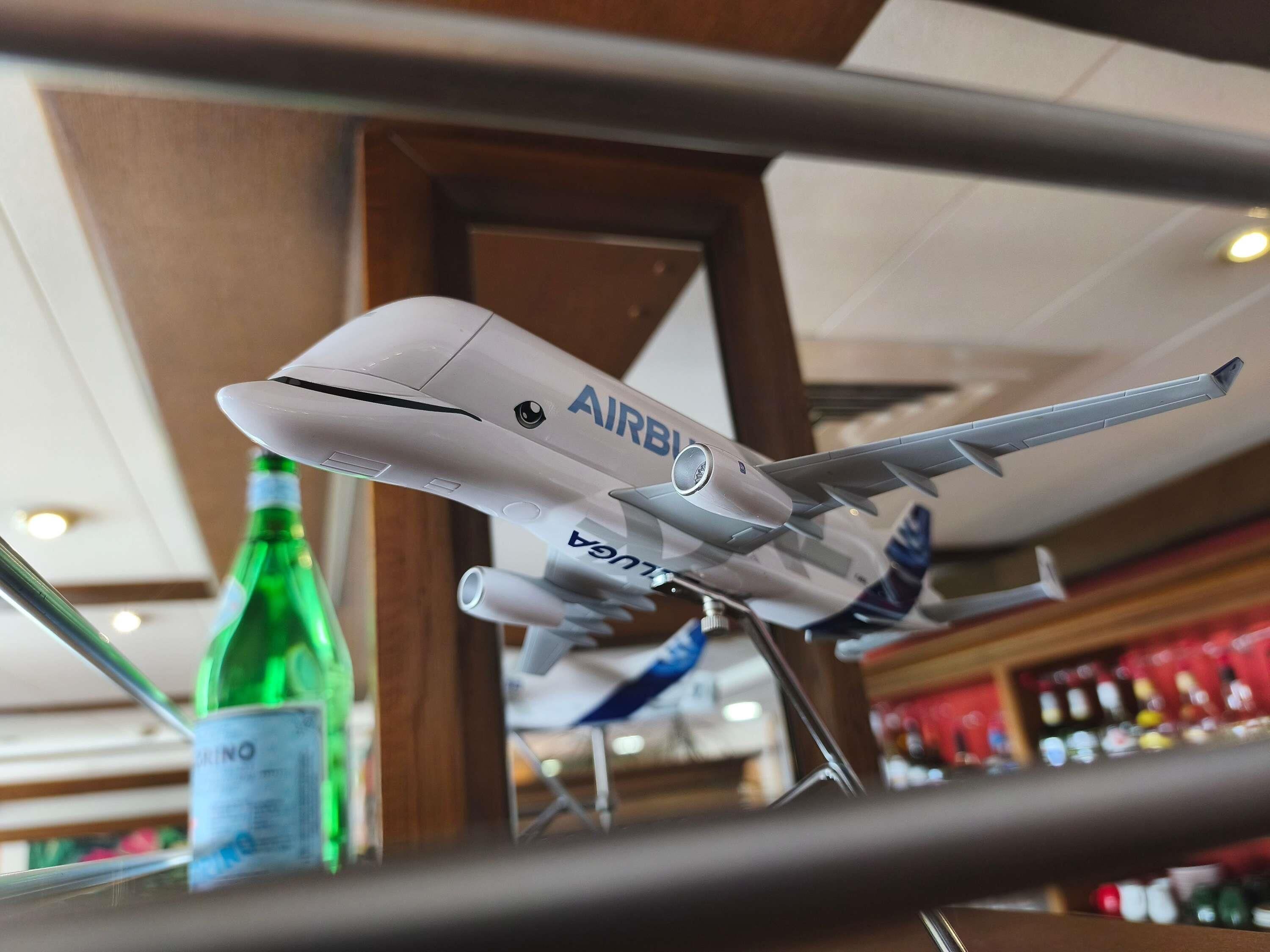 Ein Modellflugzeug mit der Aufschrift 'AIRBUS', präsentiert in einem Innenraum, im Vordergrund eine grüne Flasche.