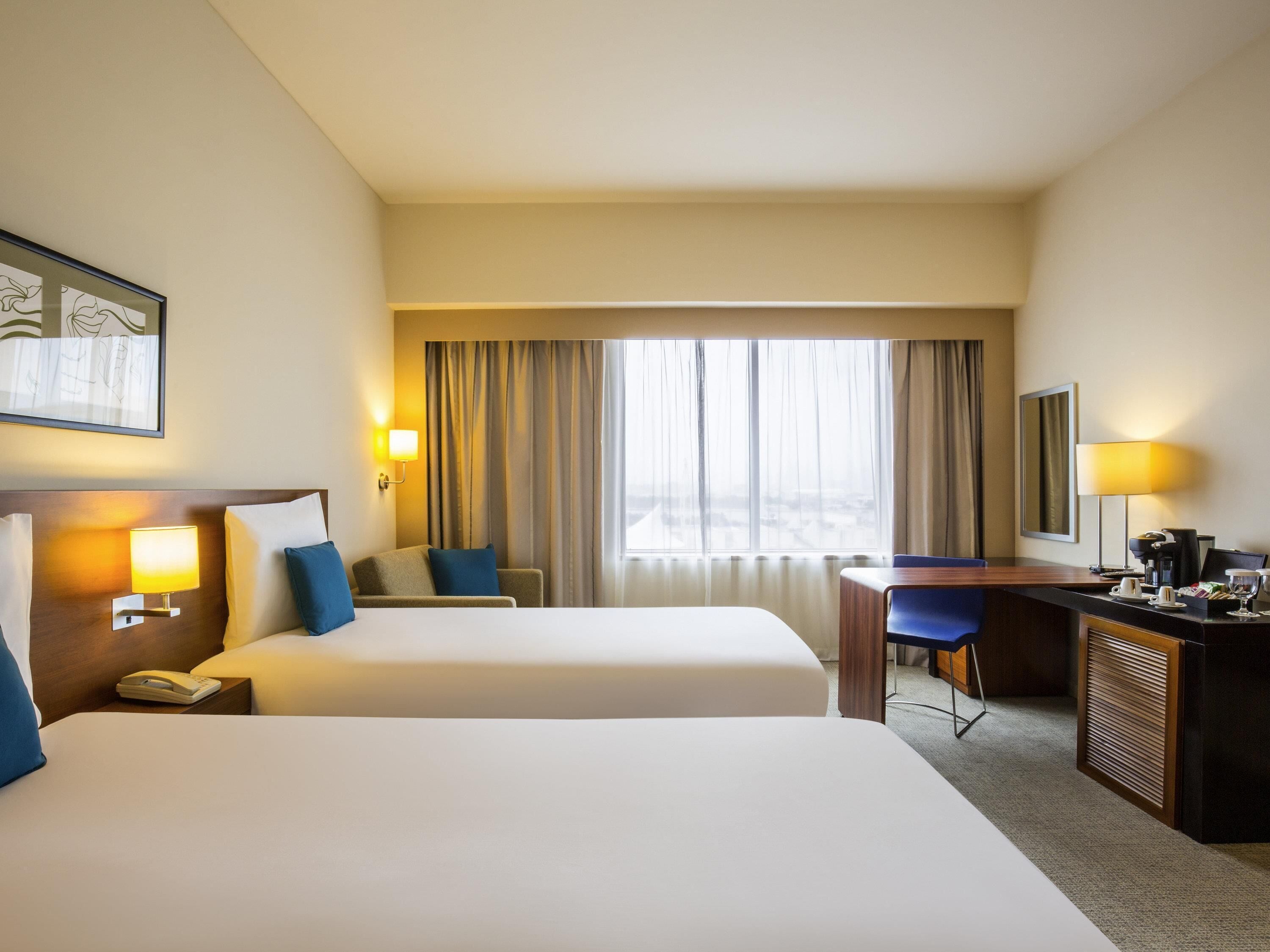 A hotel room with two beds, a desk, a chair, a telephone, and a window with curtains.