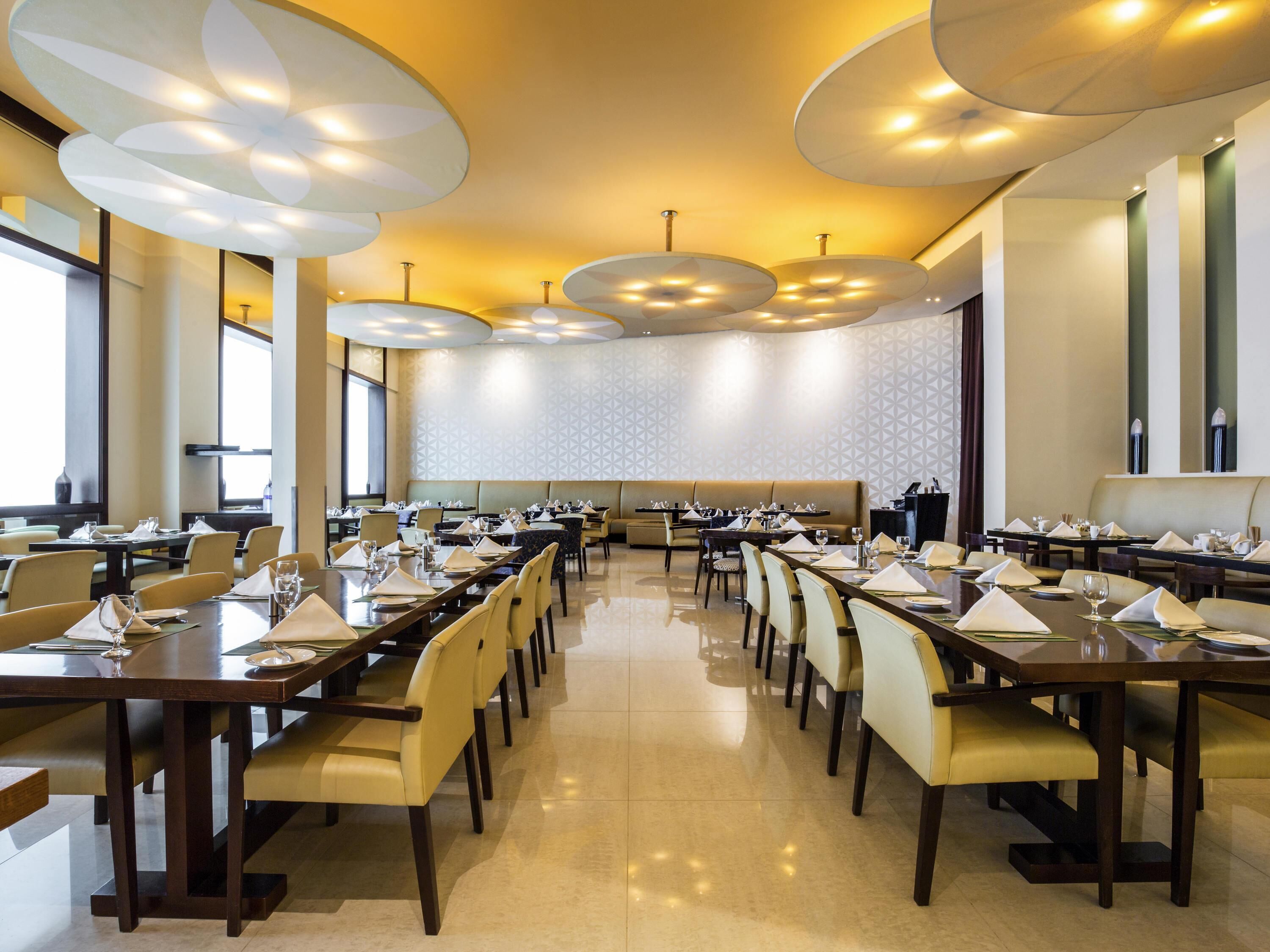 A conference room with long tables, chairs, and a high ceiling with circular light fixtures.