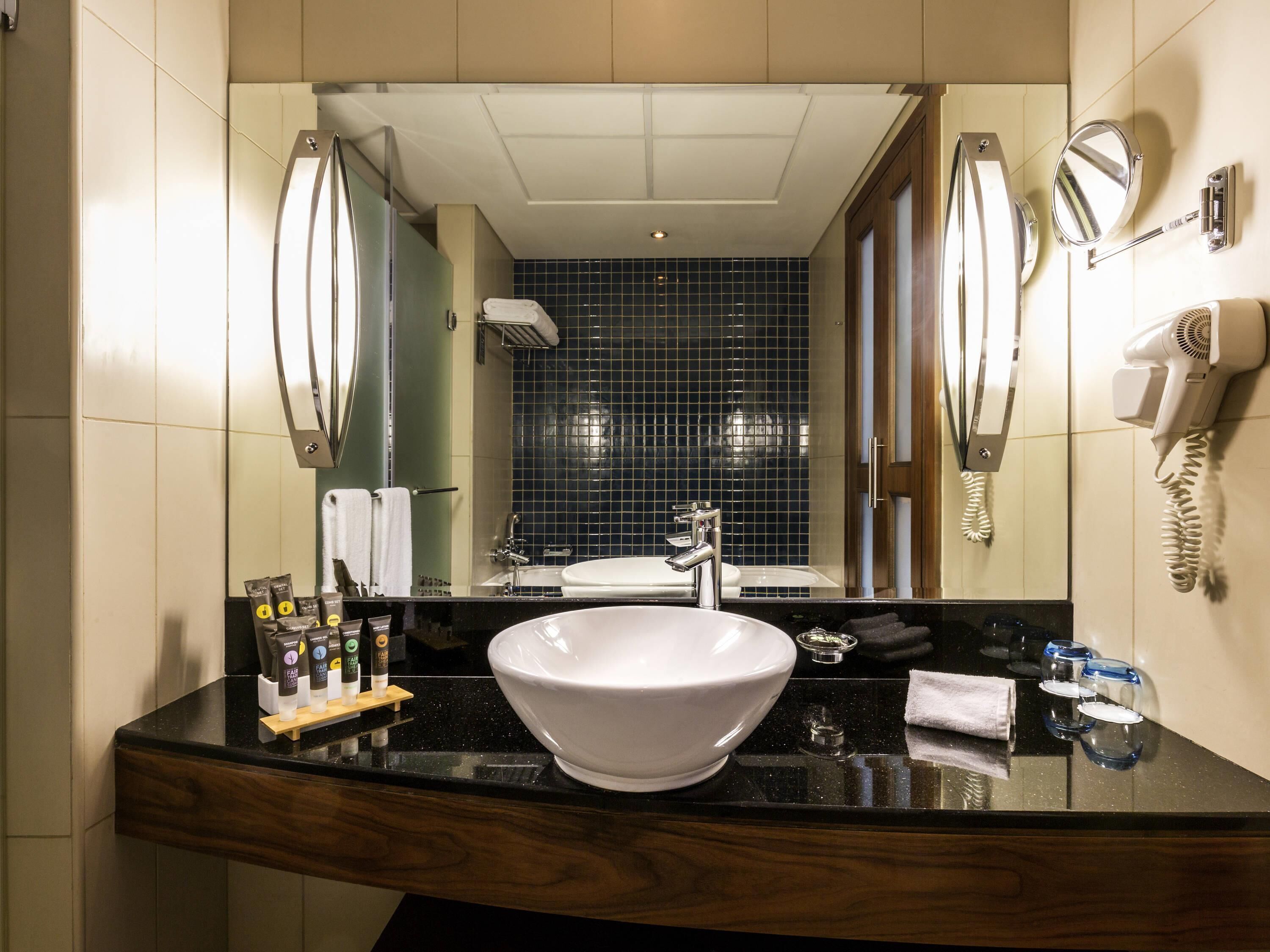 Ein Badezimmer mit einem großen Spiegel, einem Waschbecken mit weißer Schüssel, einem Föhn und Toilettenartikeln auf der Ablagefläche.