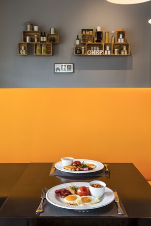 A dining table with two plates of breakfast food, a wall-mounted shelf with kitchenware, and a framed picture.