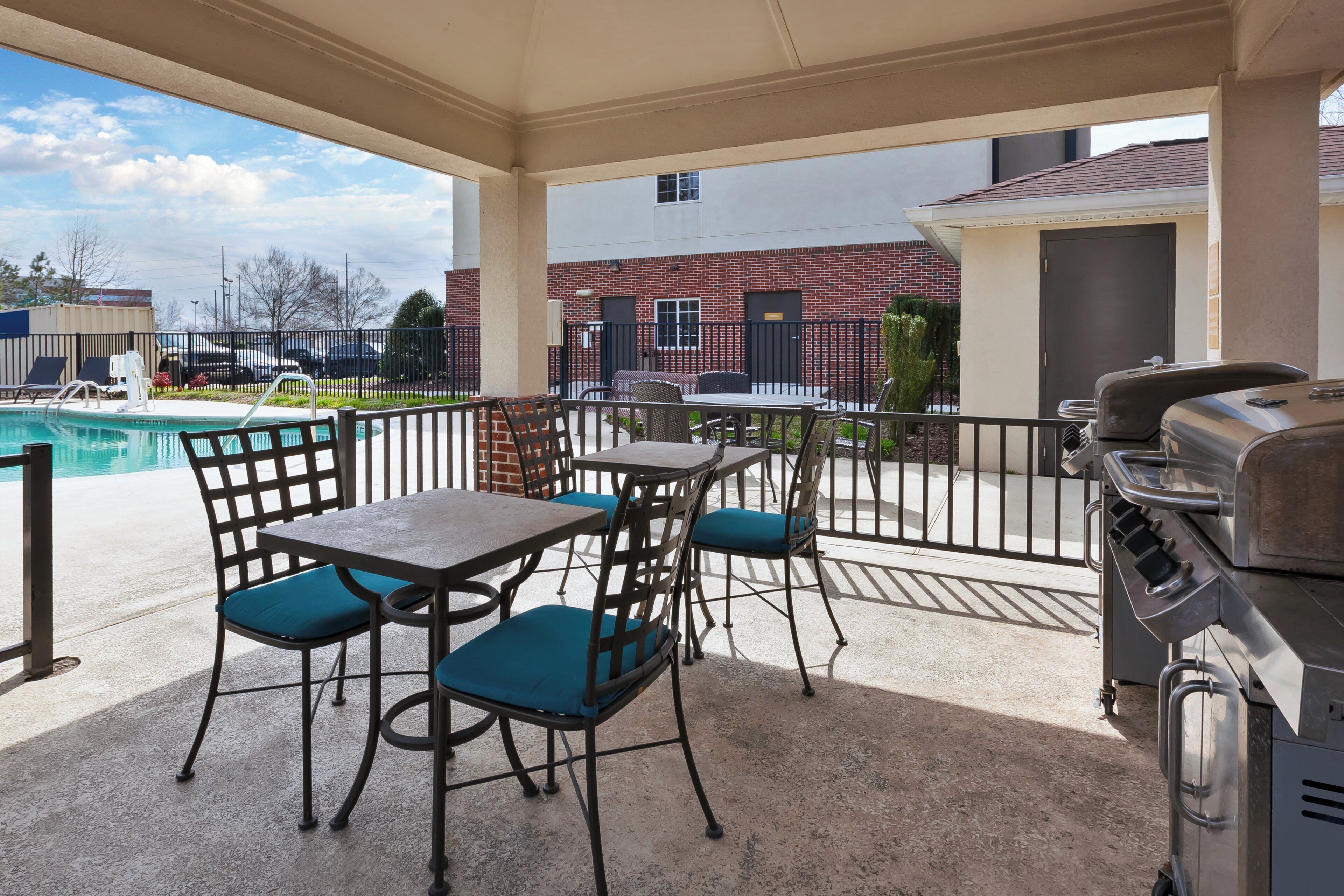 Un espacio al aire libre con patio, piscina, parrilla y mesa con sillas.