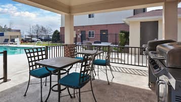 Un espacio al aire libre con patio, piscina, parrilla y mesa con sillas.