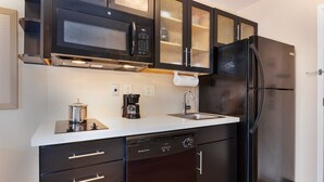 A compact kitchen with a built-in microwave, a stainless steel coffee maker, a dishwasher, and a black refrigerator.