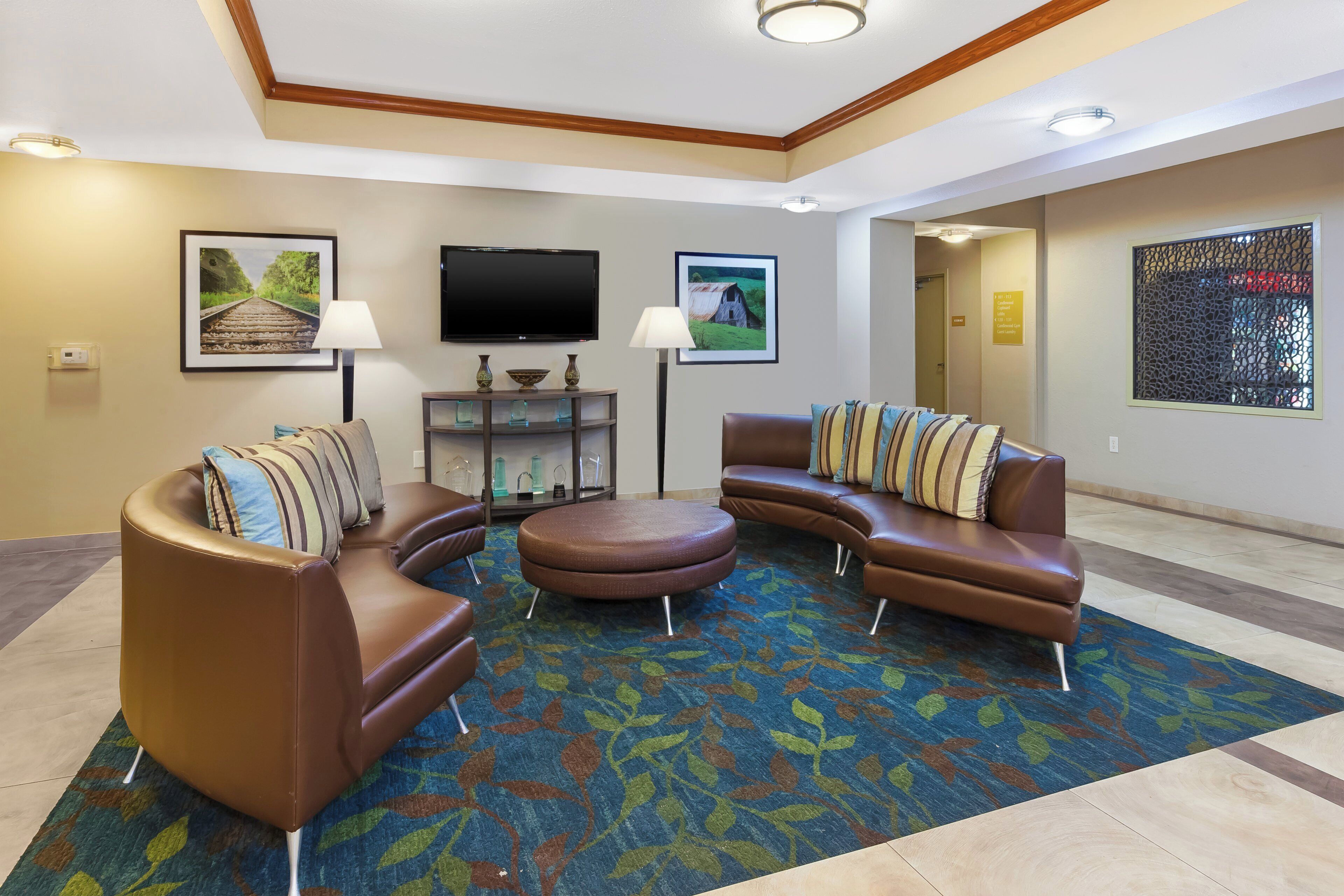 A hotel lobby with a brown leather sofa set, a flat-screen TV mounted on the wall, and a patterned carpet.