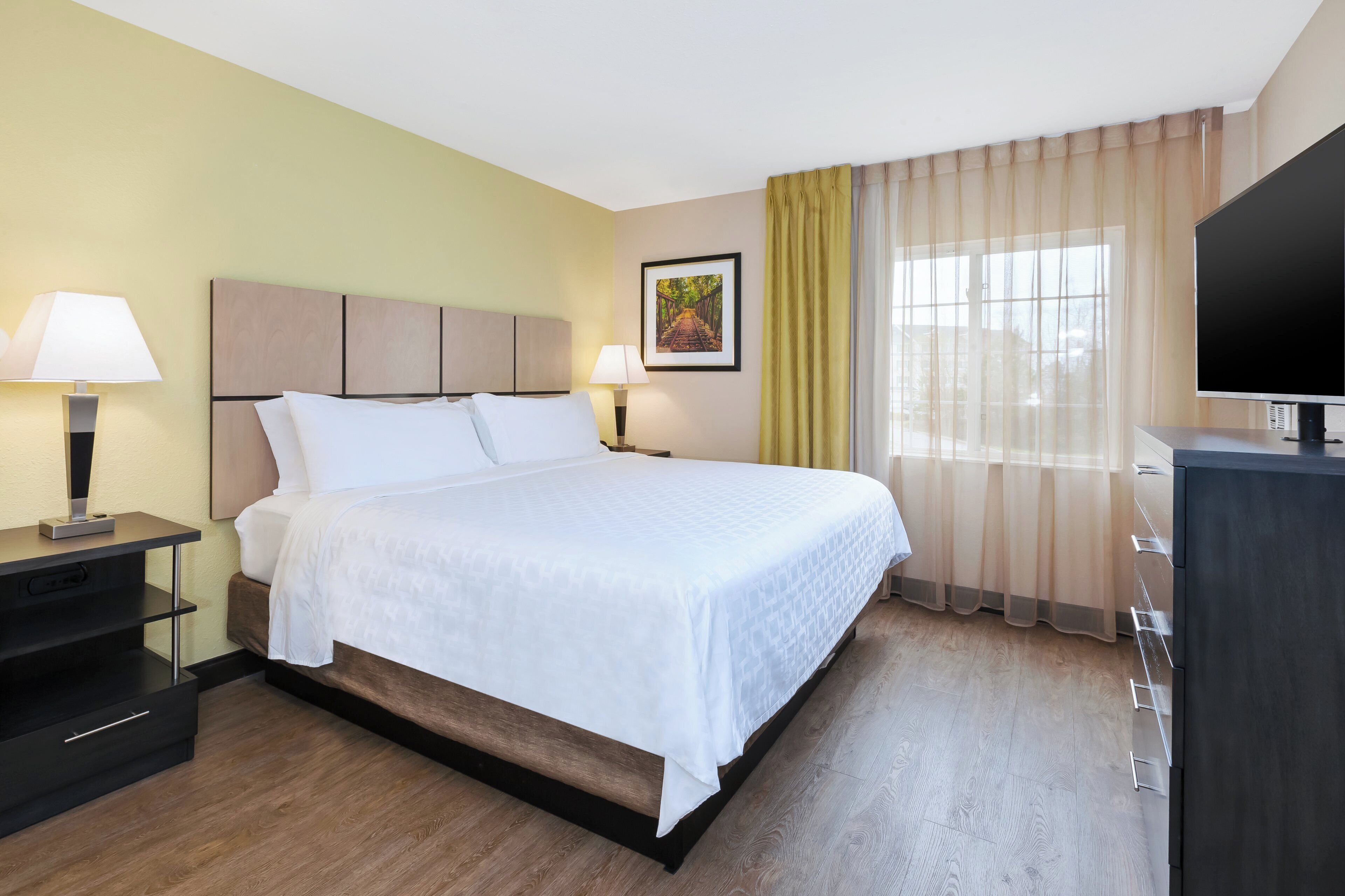 Une chambre d’hôtel avec un lit, deux tables de chevet, une télévision et une fenêtre avec des rideaux.