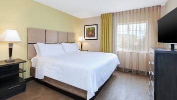 Une chambre d’hôtel avec un lit, deux tables de chevet, une télévision et une fenêtre avec des rideaux.