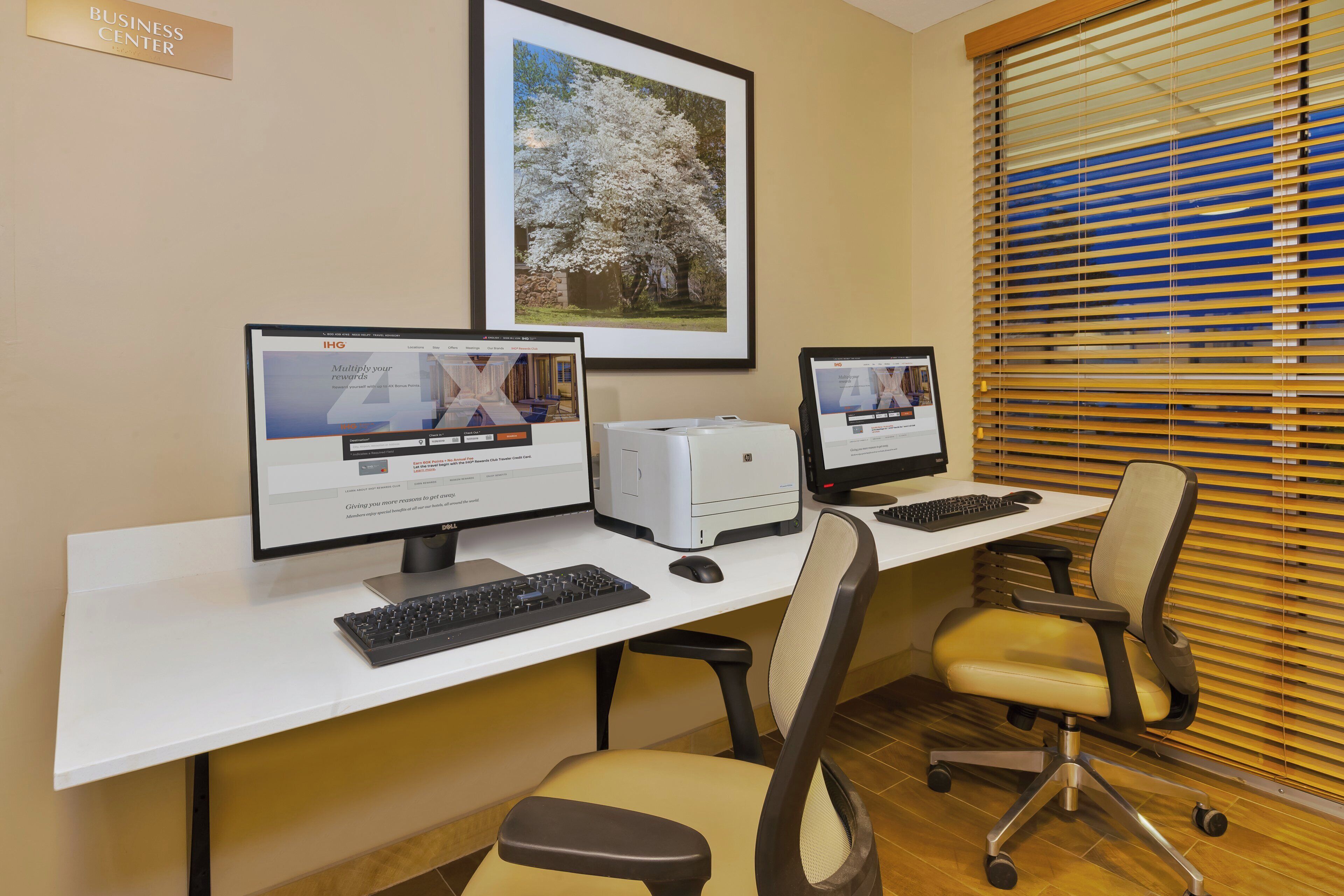 A business center with two desktop computers, a printer, and a framed picture on the wall.