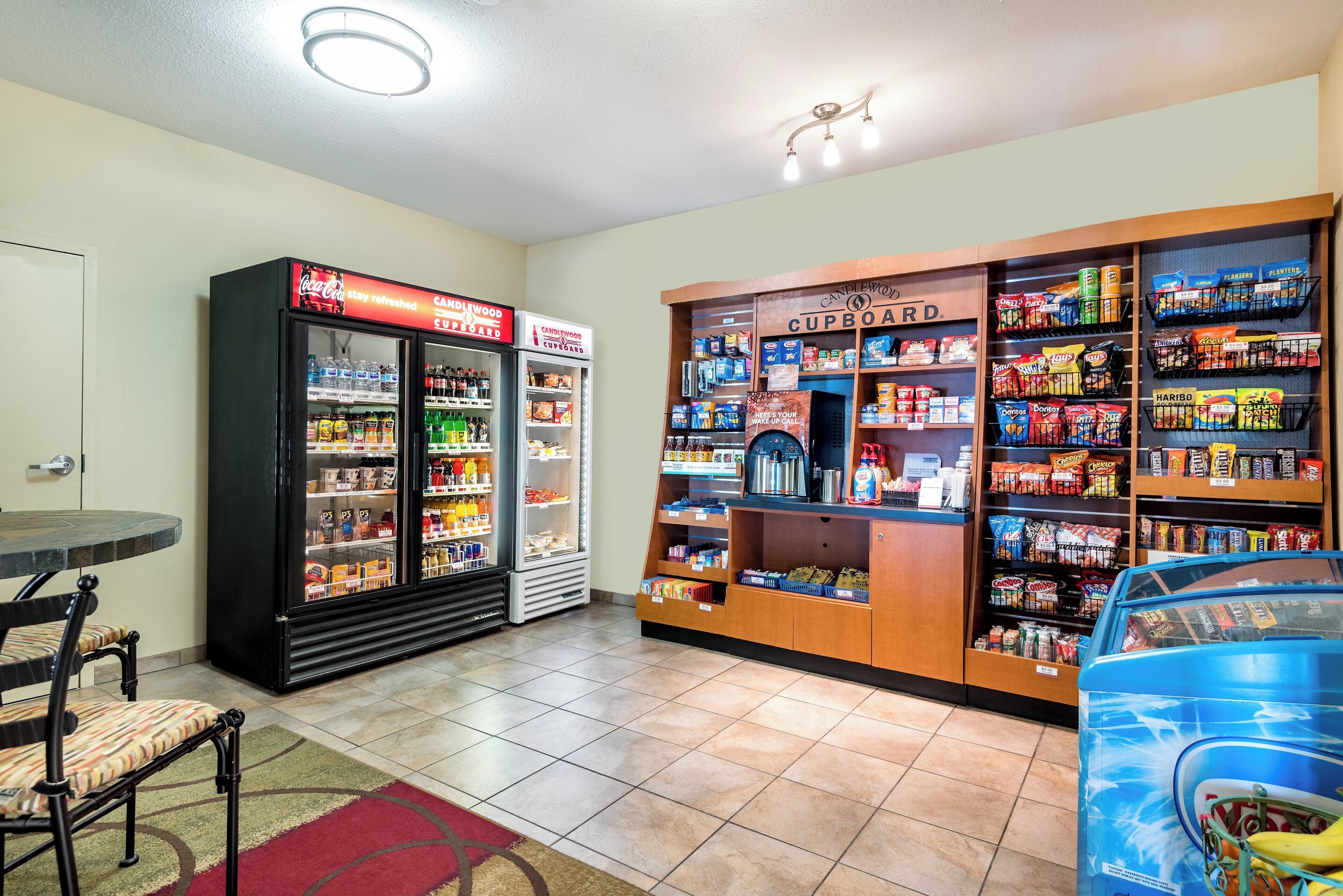 A convenience store with a refrigerator, shelves stocked with snacks, and a coffee machine.