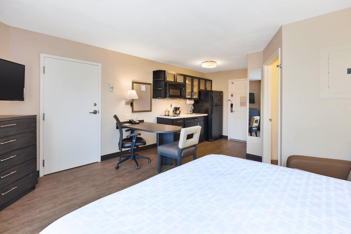 Une chambre d’hôtel comprenant un lit, un bureau avec une chaise, une kitchenette et un téléviseur fixé au mur.