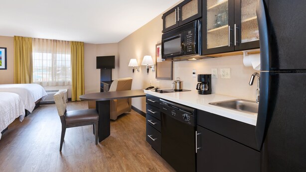 A compact hotel room with a kitchenette, a dining area, and a bed.