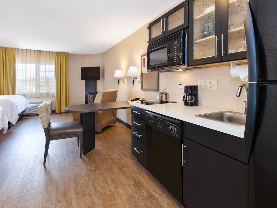 Una habitación de hotel compacta con kitchenette, comedor y cama.