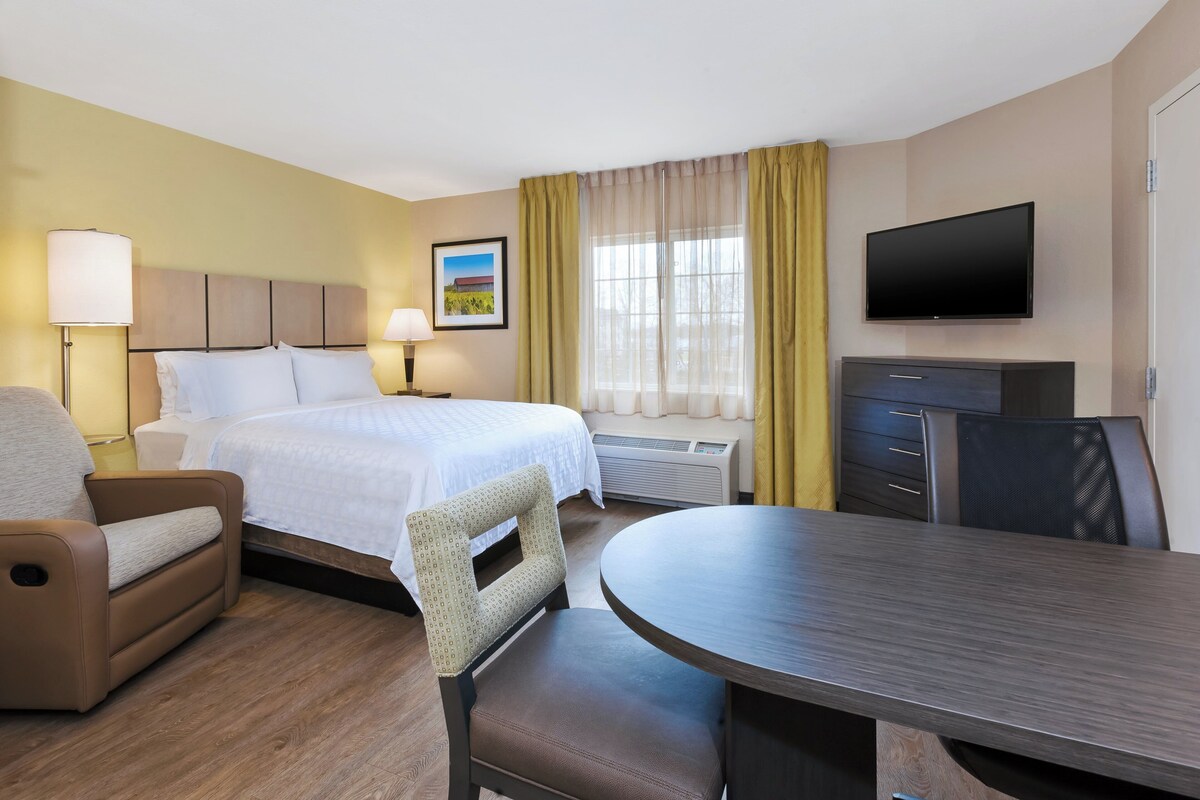 A hotel room with a bed, a desk, a chair, a TV, and a window with curtains.