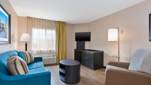 A modern living room with a blue sofa, a brown sofa, a flat-screen TV, a lamp, and a large window with curtains.