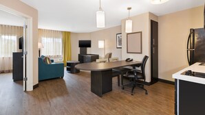 A modern hotel room with a dining area, a sofa, a TV, and a refrigerator.