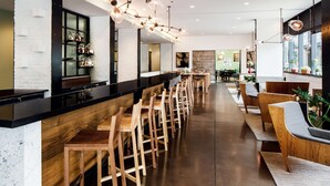 A modern bar area with wooden bar stools, a black countertop, and a variety of bottles on shelves. - ANDAZ SAVANNAH, BY HYATT (Savannah)