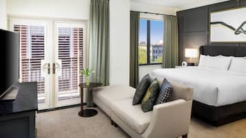 A hotel room with a bed, a sofa, a TV, a window with curtains, and a painting on the wall.