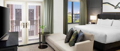 A hotel room with a bed, a sofa, a TV, a window with curtains, and a painting on the wall.