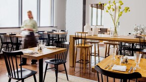 A restaurant with wooden tables and chairs, large windows, and a white brick wall. - ANDAZ SAVANNAH, BY HYATT (Savannah)