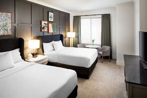A hotel room with two beds, a desk, a chair, a TV, and a window with curtains.