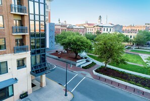 A modern building with a glass facade, a courtyard with trees, and a view of historic buildings in the background.