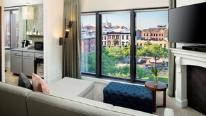 A modern living room with a large window, a flat-screen TV, a fireplace, and a view of the cityscape. - ANDAZ SAVANNAH, BY HYATT (Savannah)