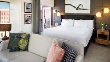 Una habitación de hotel con una cama grande, un sofá, una mesita de noche con lámpara y obras de arte en las paredes.