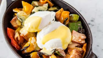 A skillet with a breakfast dish, including poached eggs and vegetables, on a marble countertop.