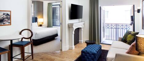 A hotel room with a bed, a TV, a fireplace, a balcony, and a dining area.