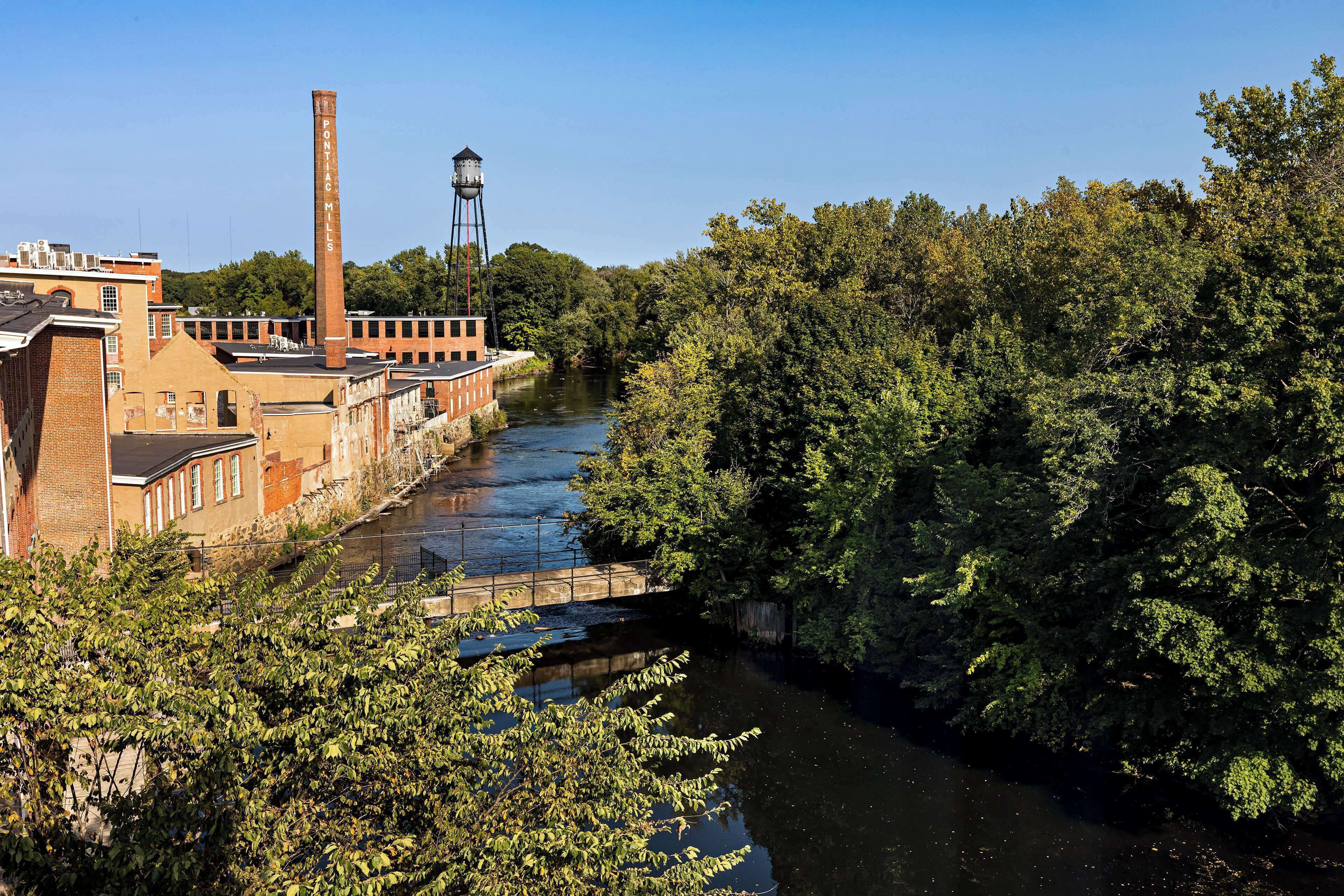 Een rivier met fabrieksgebouwen en een hoge schoorsteen aan de linkerkant.