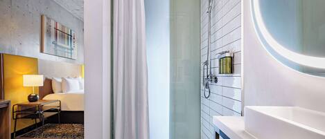 Un baño de hotel moderno con cabina de ducha de vidrio, un espejo redondo y un lavamanos blanco.