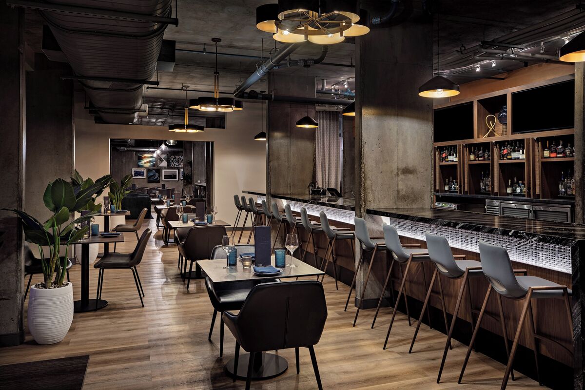 Eine moderne Bar mit Holzboden, Barhocker und einer Auswahl an Flaschen in Regalen.