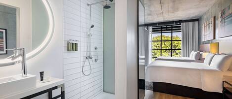 Ein modernes Badezimmer mit Dusche, Waschbecken und Spiegel. Das Zimmer verfügt über ein großes Fenster mit Blick auf Bäume.