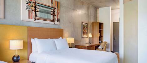 Een hotelkamer met een groot bed, twee nachtkastjes met lampen, een houten bureau en een stoel.